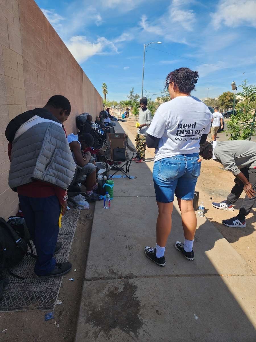 A 4TK volunteer in a 'need prayer?' shirt serving people along a sidewalk